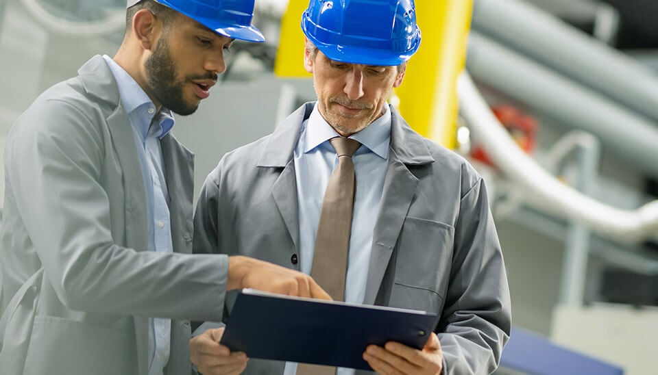 Two men in business attire and hard hats, reviewing a tablet screen