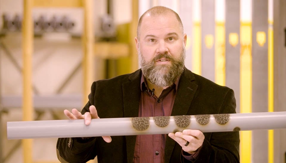 Man with beard holding a CPVC pipe wearing black suit jacket